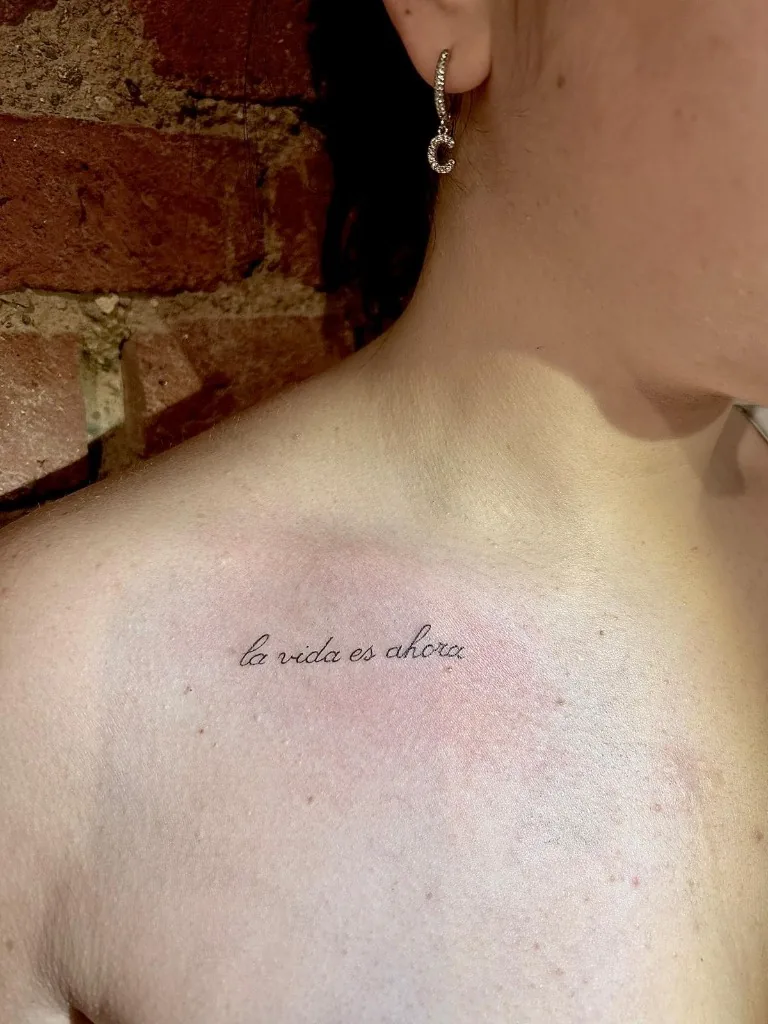 Tatuaggio lettering fine line sul petto con la scritta la vida es ahora