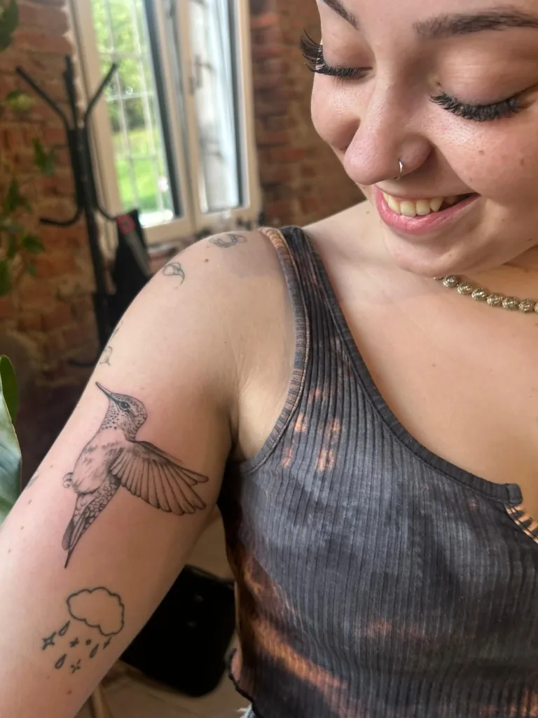 Tatuaggio illustrativo fine line di un colibrì in volo sul braccio realizzato da Anny