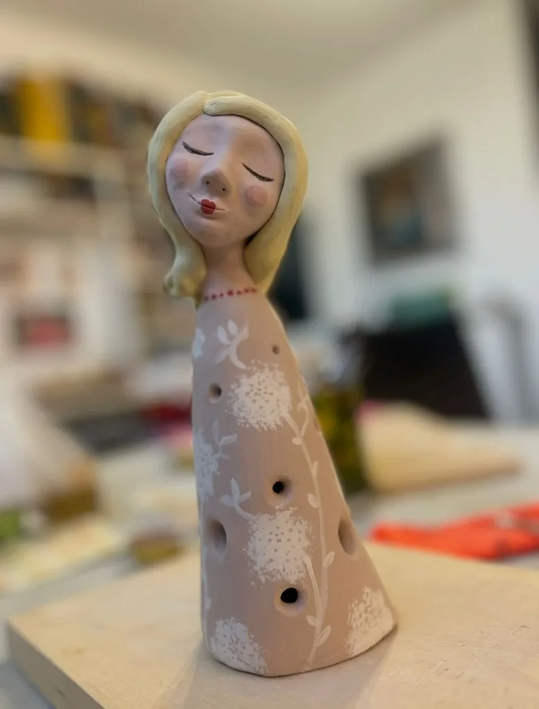 Scultura ceramica di ragazza con occhi chiusi e vestito dipinto con fiori bianchi
