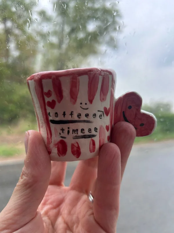 Tazzina da caffè in ceramica modellata a mano con righe rosse e manico a forma di cuore con la scritta coffee time